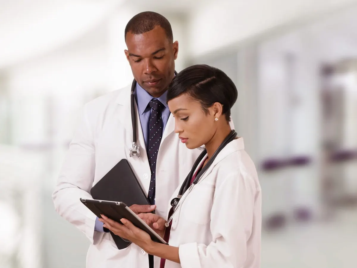 Two doctors in white coats look at a tablet together