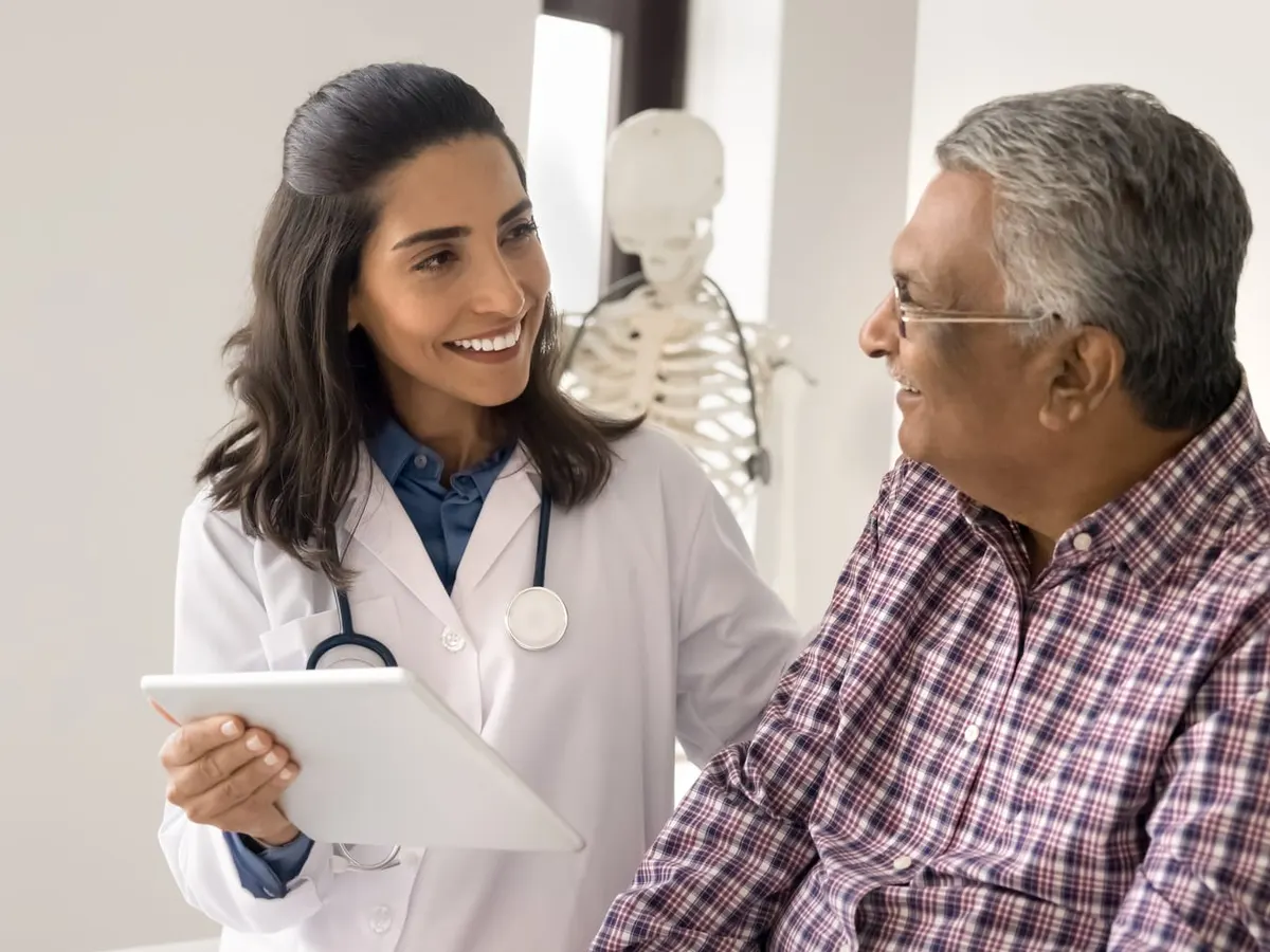 A smiling doctor holding a tablet talks with an older man