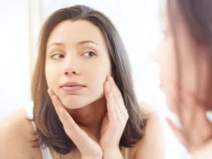 woman looking at her face in the mirror after getting rosacea treatment