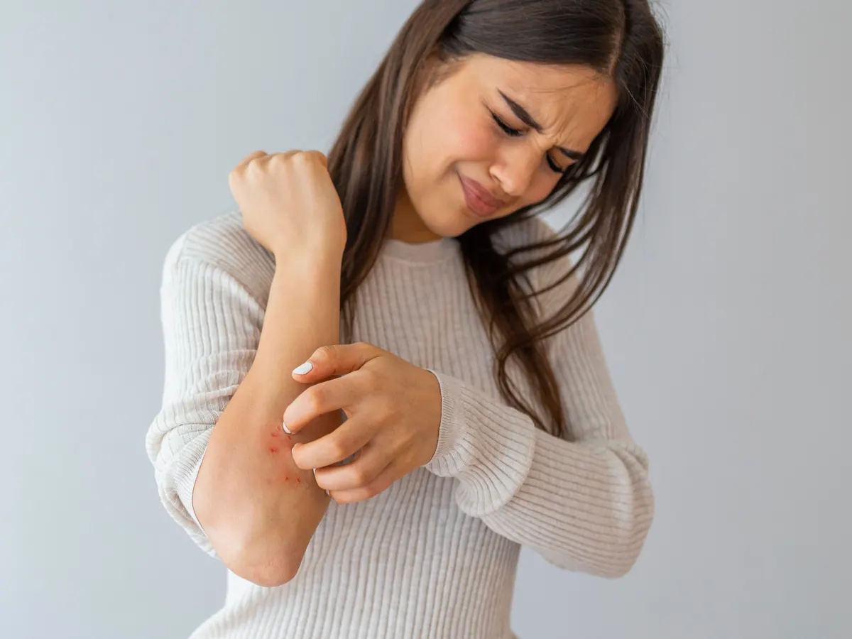 A woman winces as she scratches her forearm