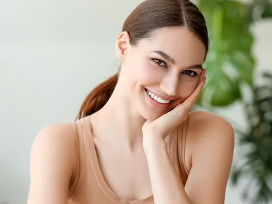 smiling woman sitting at table with bottles of essential oil in room