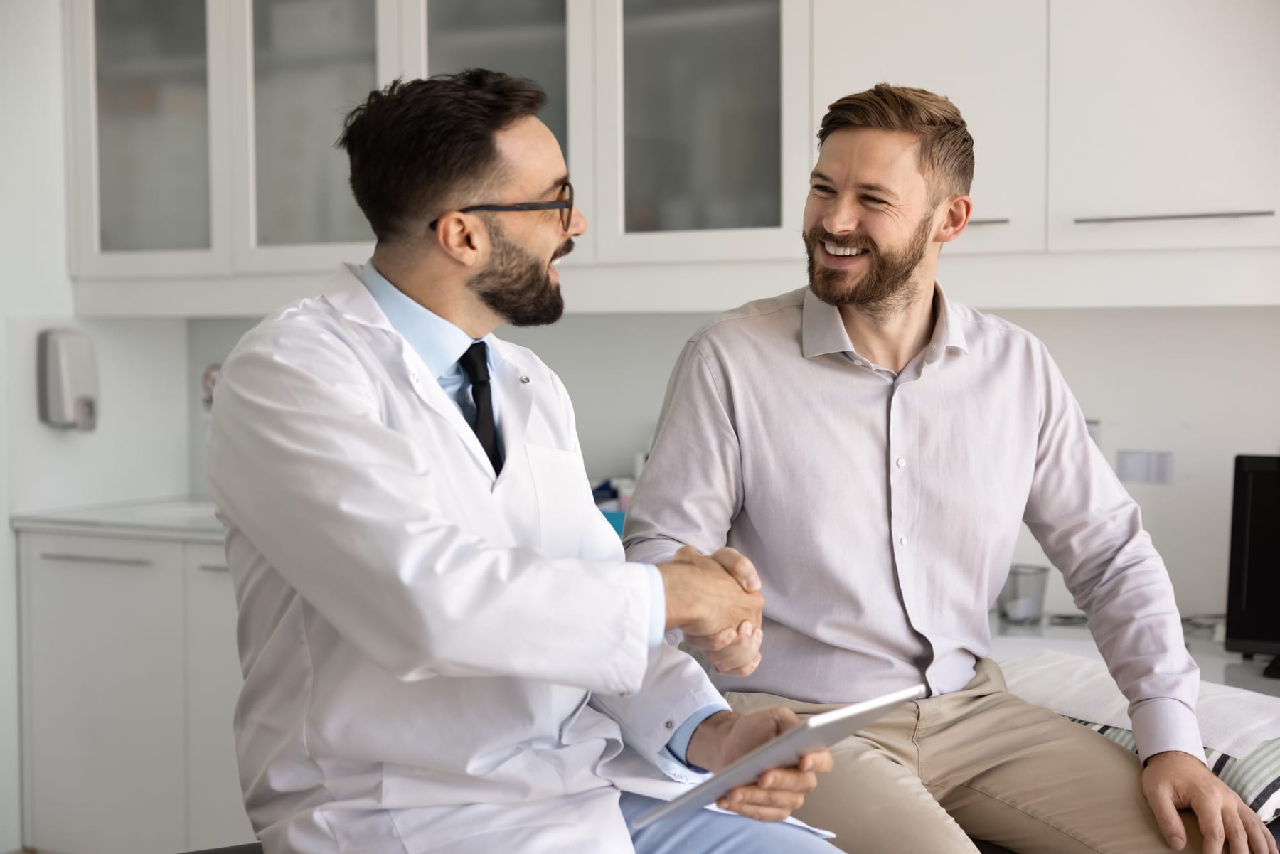 A doctor shakes hands with a smiling man in an exam room