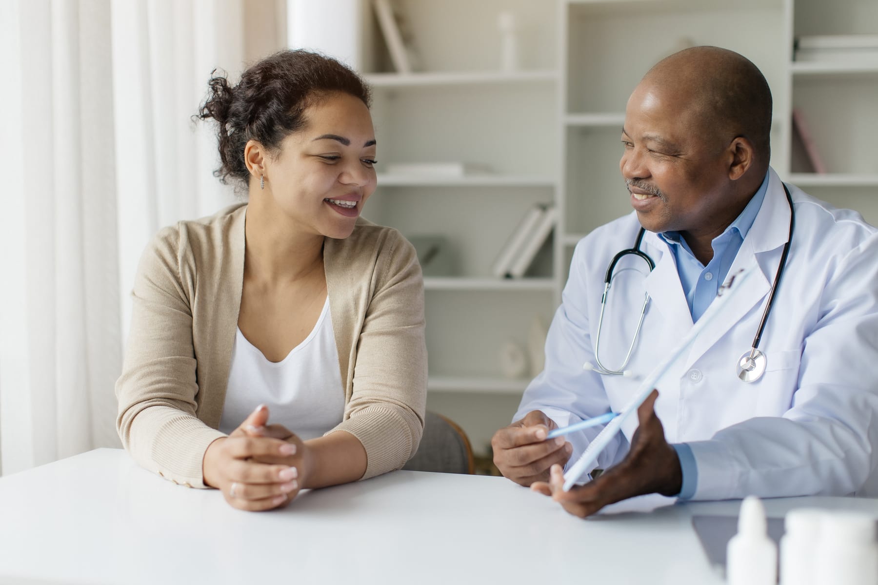 A doctor shows a smiling woman something on a tablet across a desk