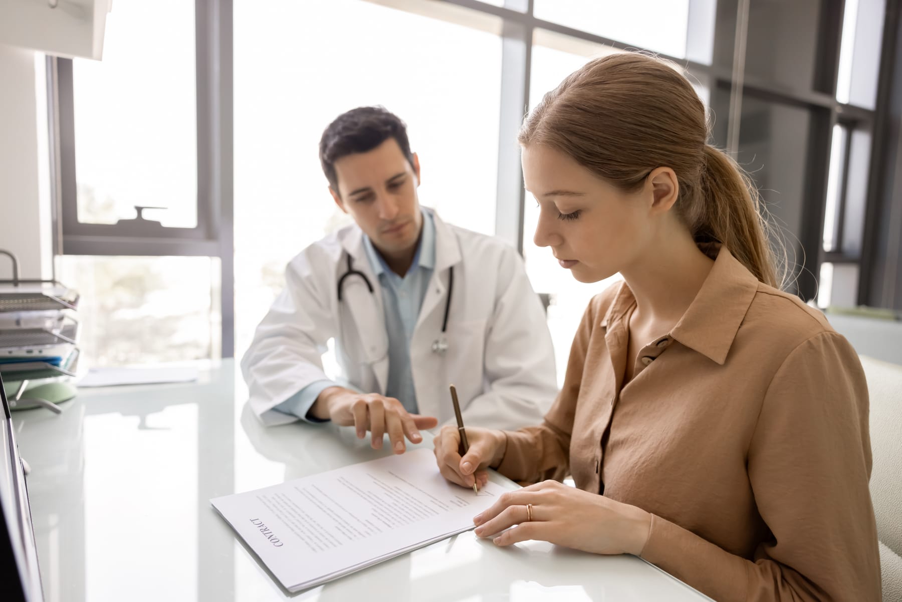 A woman signs a form at a desk while a doctor points to it