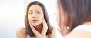 woman looking at her face in the mirror after getting rosacea treatment
