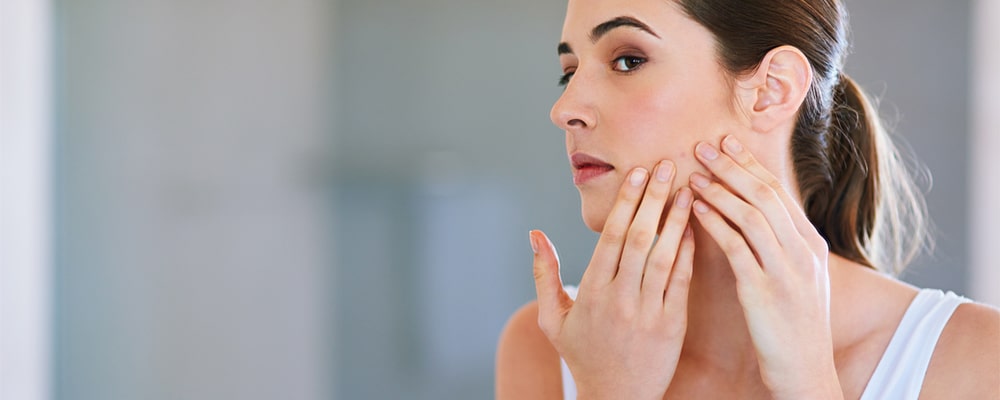 a young woman squeezing a pimple on her face