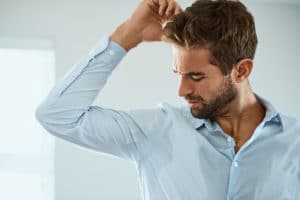 Shot of a handsome young man smelling his armpits at home