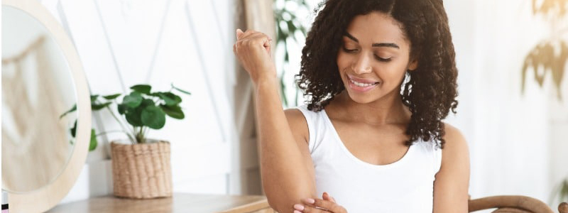 dry elbows treatment smiling black woman applying moisturising cream picture