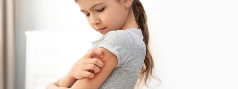 Little girl scratching arm indoors.